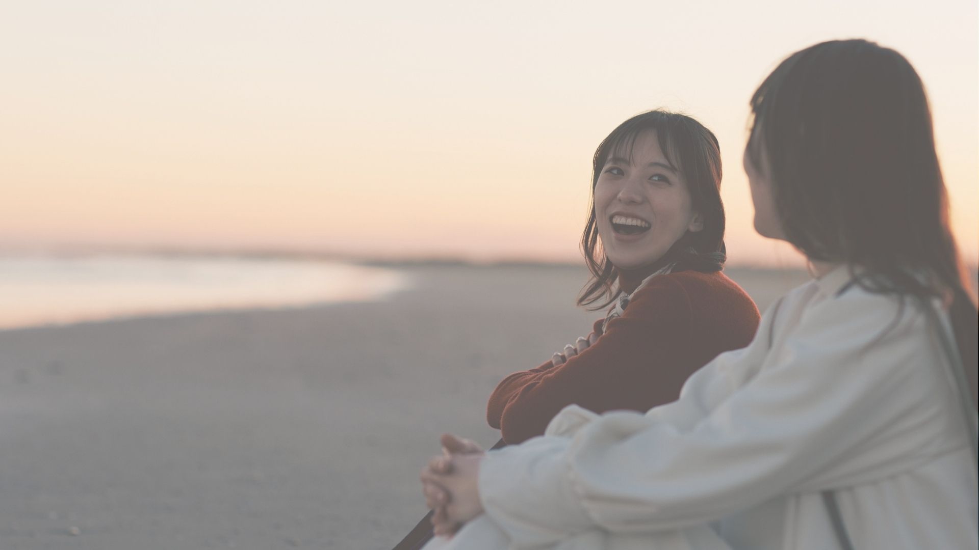 Two women sharing a laugh beside the water at sunset.
